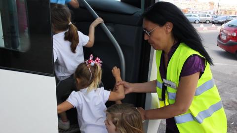 Imagen de niñas subiendo al autobus ayudadas por una trabajadora
